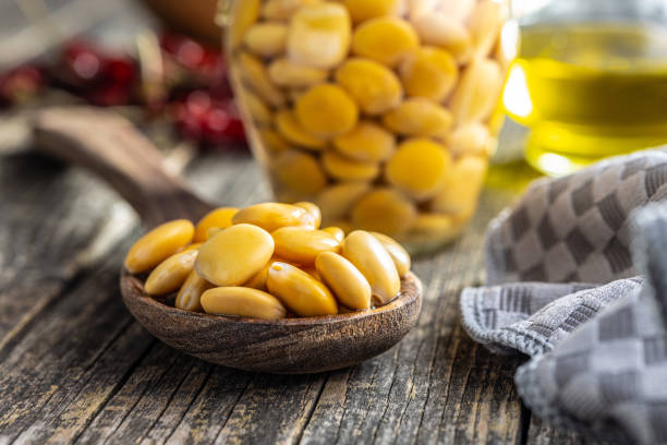 frijoles lupini en salmuera. altramuz en escabeche en cuchara sobre mesa de madera. - altramuz fotografías e imágenes de stock