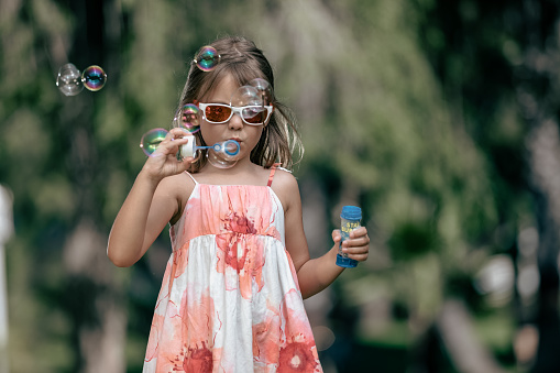 Little girl with sunglasses making bubbles in the garden