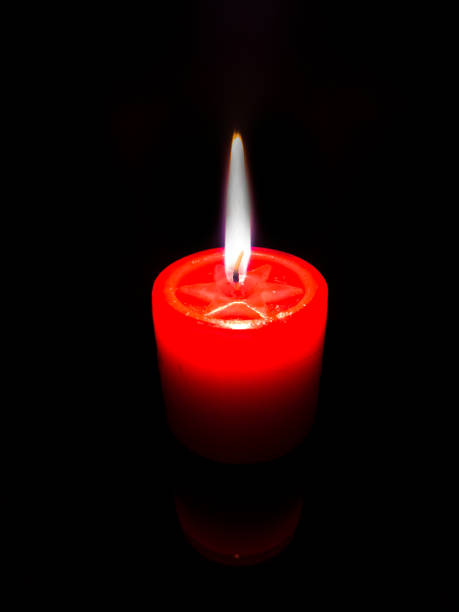 Red candle with burning flame in the dark
