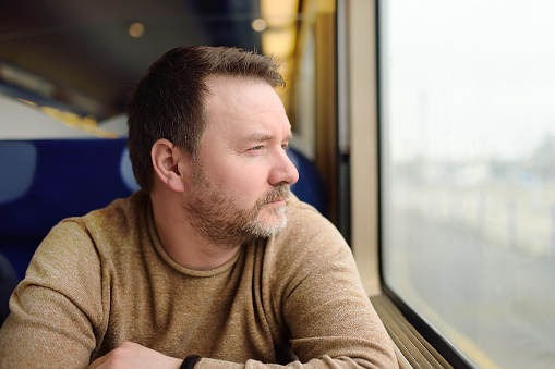 Middle age man looking out of the window of train. Passenger during travel by high speed express train in Europe