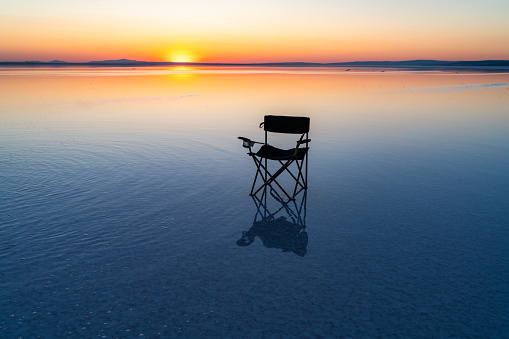 Background photo of camping chair in Salt Lake. the reflection of the camping chair falls into the water. The sun is setting on the water horizon. Shot with a full-frame camera in daylight.