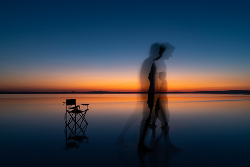human reflections falling into the Salt Lake of time in the blue hour at sunset. the reflection of the camping chair falls into the water. The sun is setting on the water horizon. silhouette of young men standing. Shot with a full-frame camera in daylight.