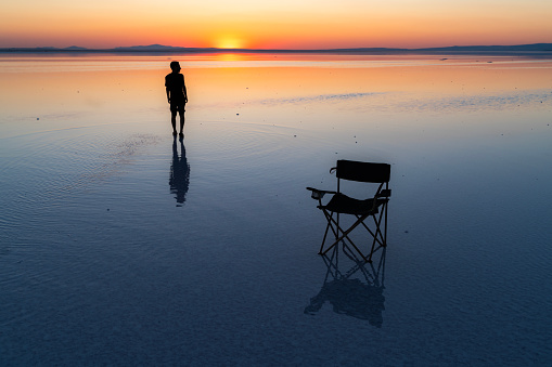 human reflections falling into the Salt Lake of time in the blue hour at sunset. the reflection of the camping chair falls into the water. The sun is setting on the water horizon. silhouette of young men standing. Shot with a full-frame camera in daylight.