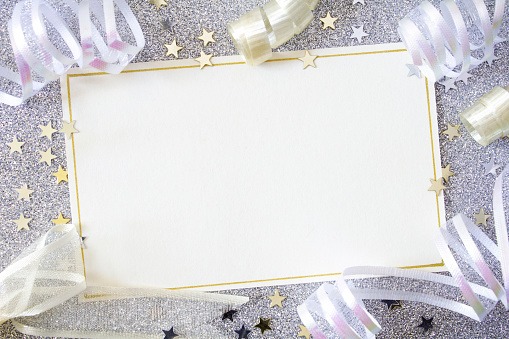 A blank card with white copy space, on a silver glitter background surrounded by ribbons and stars.