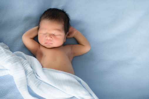 A newborn mixed race Asian Caucasian baby boy sleeps on blue blankets. With copy space