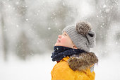 Cute little boy in yellow winter clothes walks during a snowfall