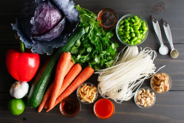 Uncooked rice noodles and fresh vegetables and spices on a wooden table