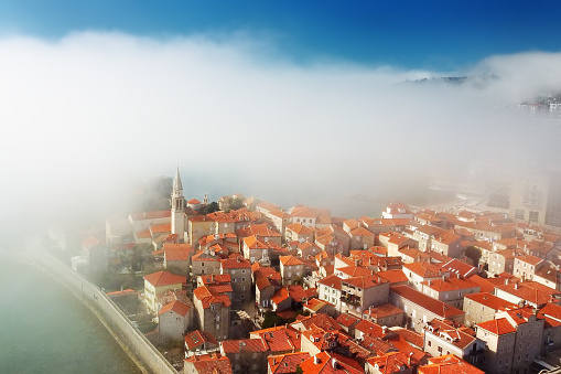 Mysterious drone view of the ancient city of Budva during heavy cloud cover. Old medieval city with red roofs in Montenegro on the sunset. Budva is the most popular resort town in Crna Gora