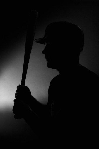 a silhouette / back lit of a baseball player holding a bat and wearing a helmet. 