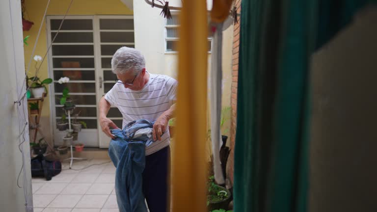 Senior man reverting pants from the inside out after drying on hanger, older person doing domestic chore routine by straightening jeans