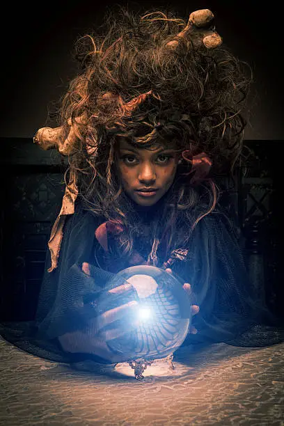 Voodoo Priestess with magic ball. This stock image has a vertical composition on a dark background.