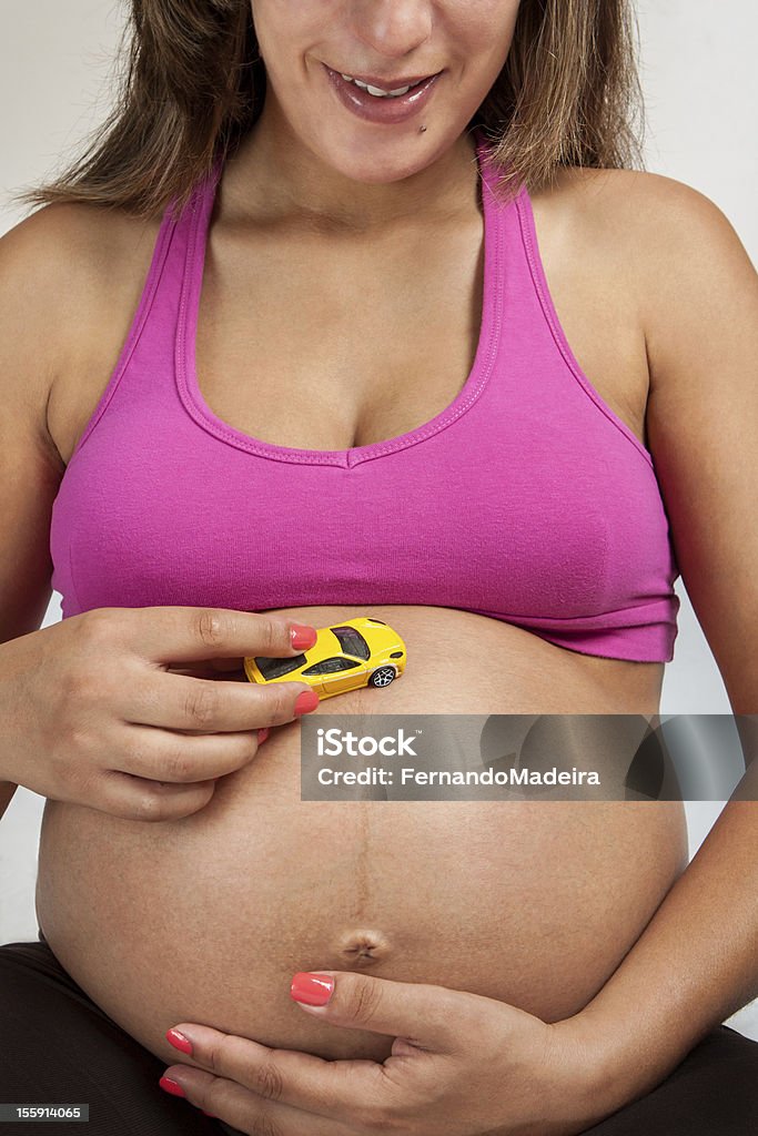 Femme enceinte heureuse, jouant avec un jouet voiture sur son ventre - Photo de Abdomen libre de droits