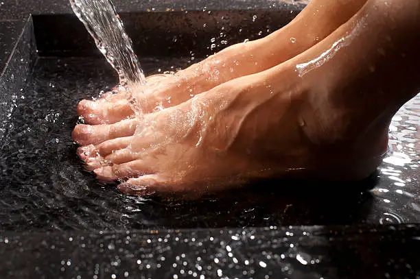 Woman's feet in water. splashing as the water falls from the tap