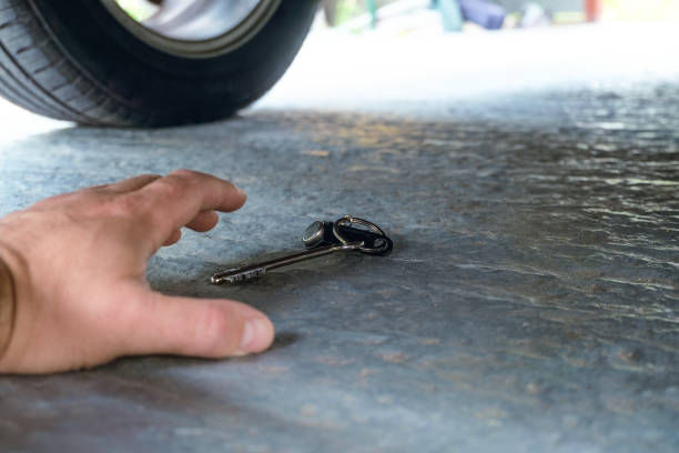 istock Hand reaches for the keys that fell under the car. Selective focus on key. 1559170031