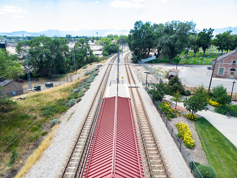 From high above, the rail transit station is a stunning sight on a warm summer day, boasting elegance and order. Expertly curated gardens and landscaped areas encircle the well-constructed platforms, complete with sheltered seating to accommodate passengers comfortably while they await their trains. The distant mountains add a touch of natural beauty to the scene. Strategically positioned within the vast urban landscape, this public transit station serves as a vital link in the city's transport infrastructure, harmoniously blending functionality and aesthetics.