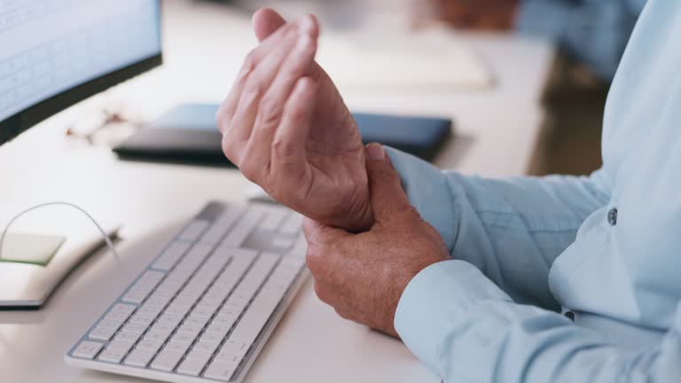 Hand, senior man with arthritis and pain from computer, desk, and massage wrist or physical therapy for carpal tunnel injury. Elderly businessman, ache in joint and sore hands working on keyboard