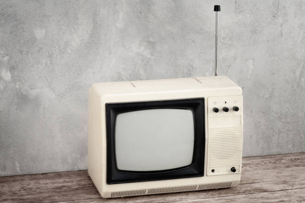 istock Vintage analog small TV set stand on wooden floor front grey concrete wall. 1559319632