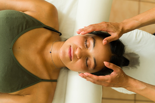 Relaxed mexican young woman lying on the massage table getting a reiki energy treatment at the alternative wellness center
