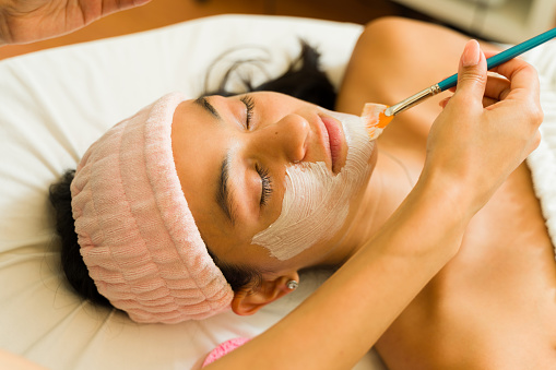 Attractive young woman at the beauty spa getting a facial mask and skin care treatment while relaxing