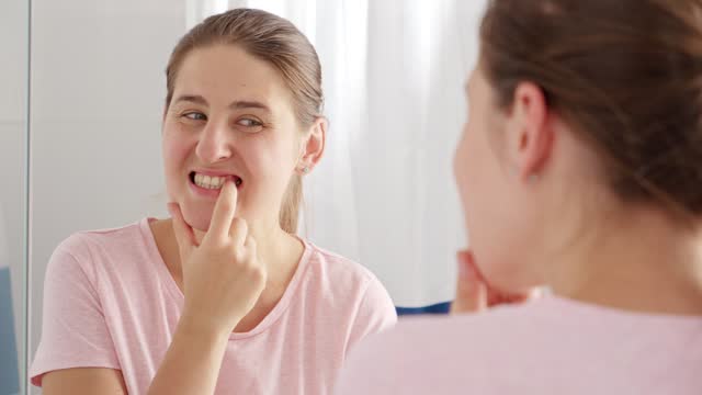 Portrait of smiling young woman looking for plaque and caries on her teeth at bathroom. Concept of teeth health, self checking mouth and oral hygiene