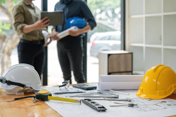 istock Concept of engineering equipments of protective helmet for competent engineer on piles of paper works. Blurred image of engineer working together at the desk 1559520468