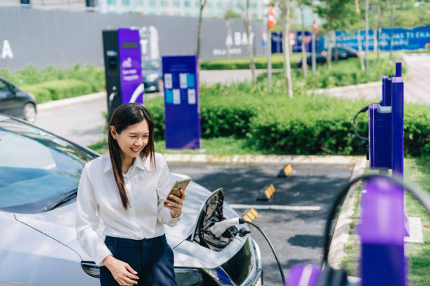 istock Woman charging electric vehicle and using smart phone 1559525609