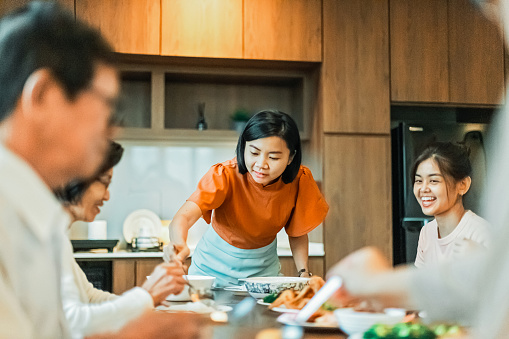 Asian Chinese daughter is serving foods to her mother’s plate during the family dinner.