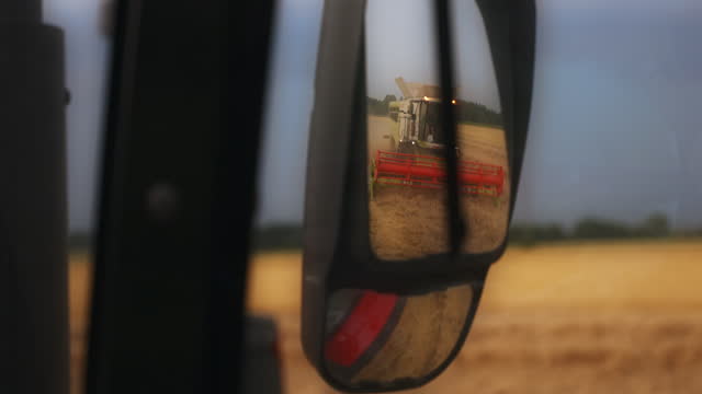 SLO MO Harvest Reflections: Tractor Rear-View Mirror Captures Combine Harvester in Wheat Field