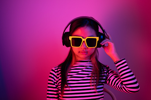 Portrait of an Asian girl wearing sunglasses and listening to music with blue and red neon lights.