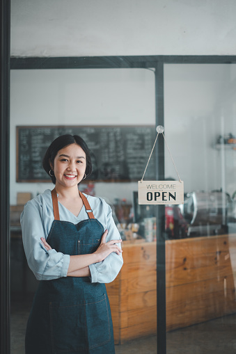 Portrait of happy waitress standing at restaurant entrance with open sign, Portrait of young business woman attend new customers in her coffee shop.