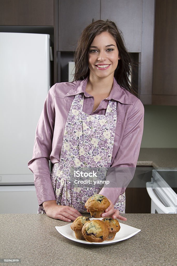 Showing muffins Young woman wearing an apron showing her blueberry muffin on a tray Adult Stock Photo