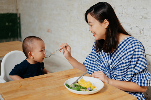 An Asian Chinese woman feeding scrambled egg to her baby boy in a cafe