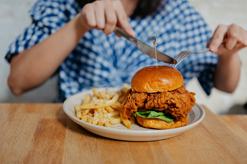 Close up shot of an Asian woman eating crispy chicken burger in a cafe