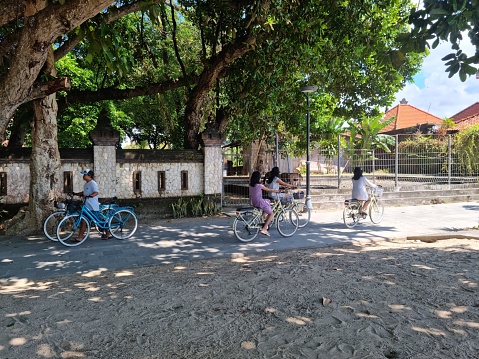 Sanur, Bali - July 16, 2023: Some people cycling with bicycle a long Sanur beach during mid hot sunny day
