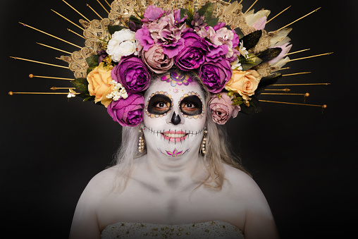 Studio portrait of woman in catrina makeup wearing wedding dress. Sugar skull make up.
