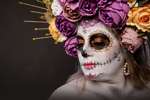 Studio portrait of woman in catrina makeup wearing wedding dress. Sugar skull make up.