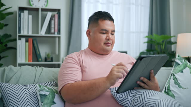 Young large build man enjoy to use tablet and digital pen in living room