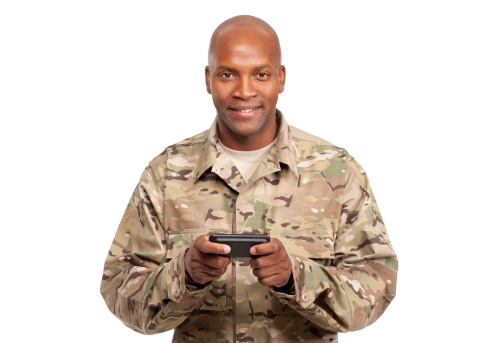 Smiling serviceman looks up at the camera while holding a smart phone
