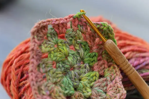 Closeup detail of crochet work with a colourful skein of organic natural handspun and handdyed merino sheep wool, silk, linnen mix yarn fleece, spun on a traditional spinning wheel