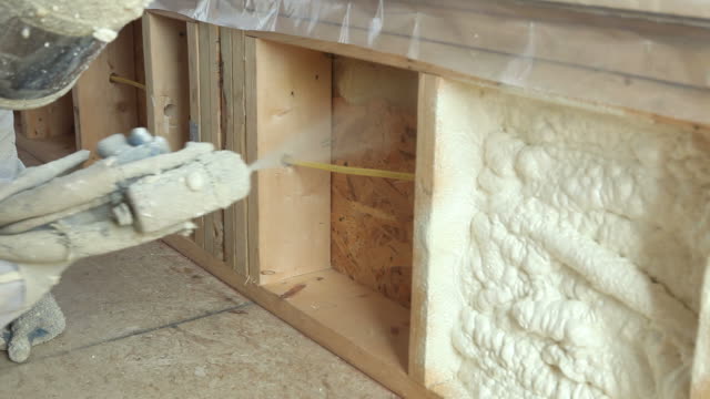 Construction Worker Spraying Expandable Foam Insulation Between Wall Studs