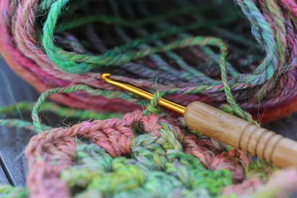 Closeup detail of crochet work with a colourful skein of organic natural handspun and handdyed merino sheep wool, silk, linnen mix yarn fleece, spun on a traditional spinning wheel