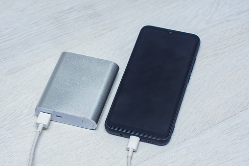 The smartphone is being charged using a portable charger on a wooden table