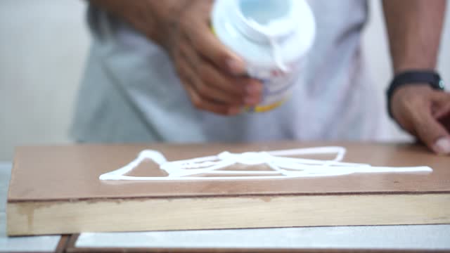 Professional technician applying glue on plywood to make canvas picture frames