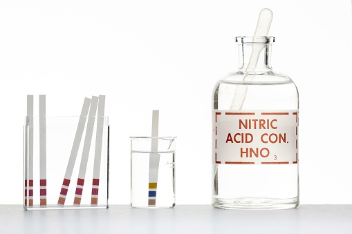 A white background with test strips for testing the pH level and a bottle of nitric acid