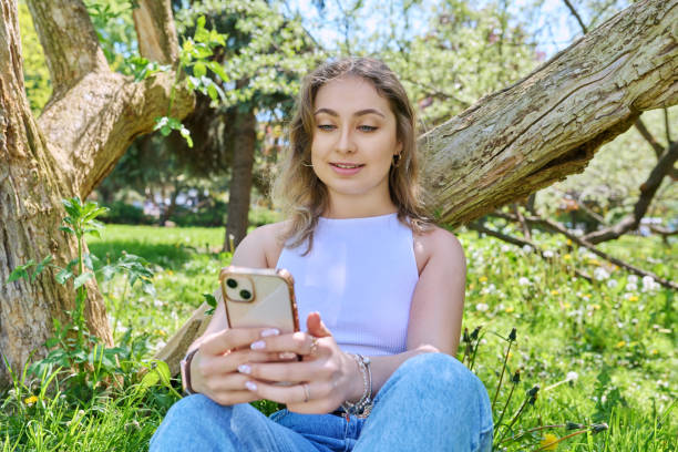 istock Young female sitting on grass in park, relaxing with smartphone 1559920283