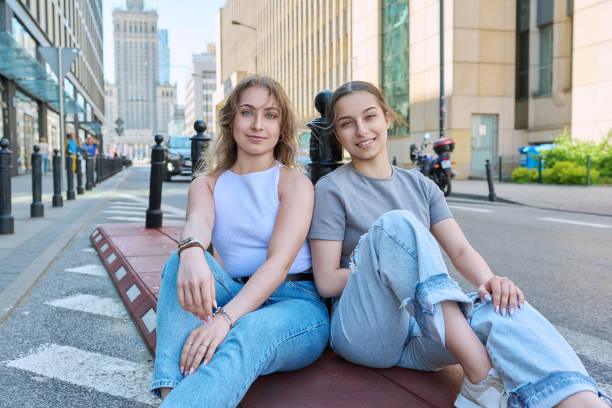 istock Two smiling female students looking at camera, modern urban style, road, buildings background 1559920997
