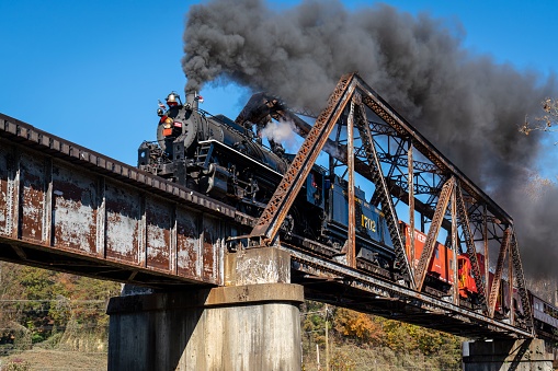 Bryson City, United States – October 20, 2022: A vintage train chugging across a bridge over a scenic landscape in Bryson City, United States.