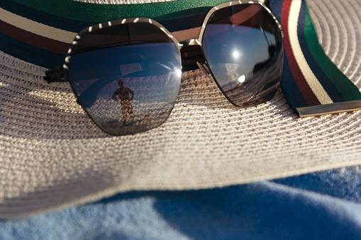 A women's straw hat and sunglasses close-up on a beach towel. Vacations and accessories concept.