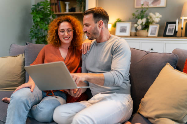 istock Handsome man sitting at home and using his laptop while his girlfriend watches 1559980335
