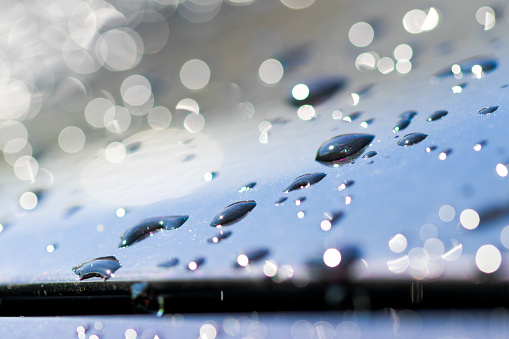 Rain droplets on a glistening metal surface glistening in the sunshine with a bokeh effect in the background, car bonnet, rain, individual droplets